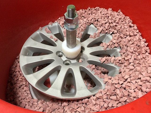 Alloy wheel being polished in ceramic finishing media inside a vibratory bowl